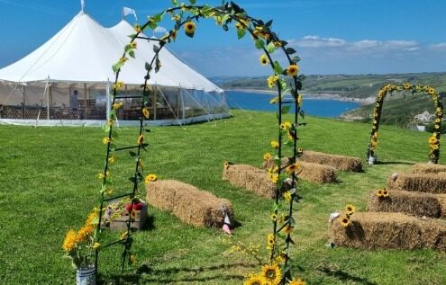 Pretty image of Our 12x24m Celeste Pole Sailcloth Marquee at Worsell Barton Farm. Hay bails and wedding ceremopmny archway in the foreground